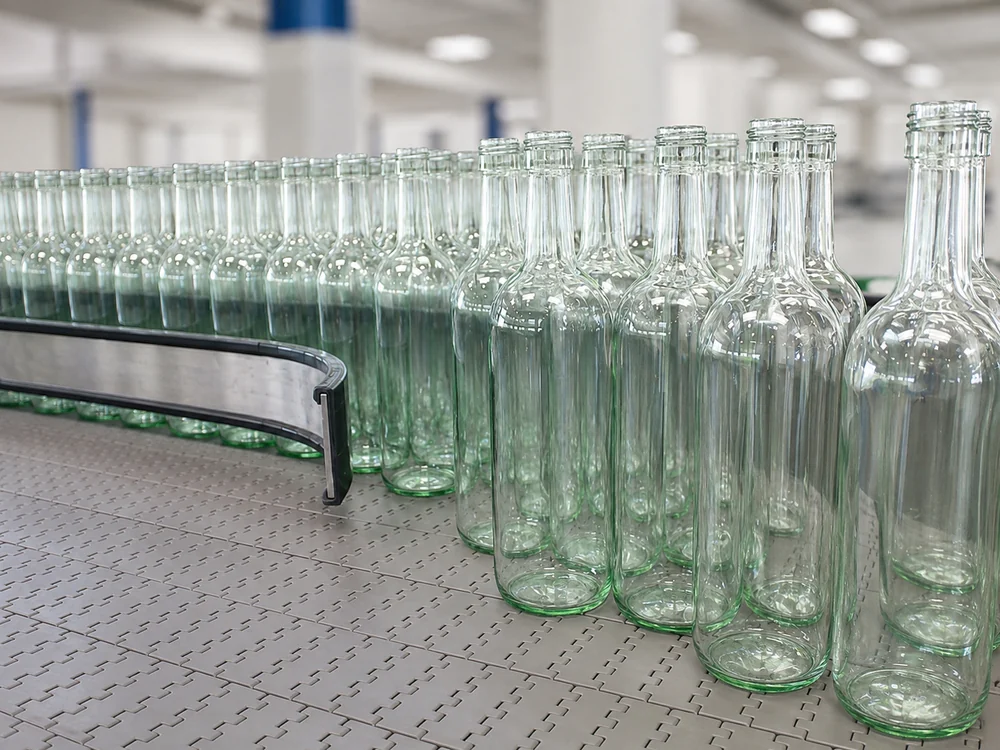 Rows of empty glass bottles guided along a conveyor toward bottle preparation