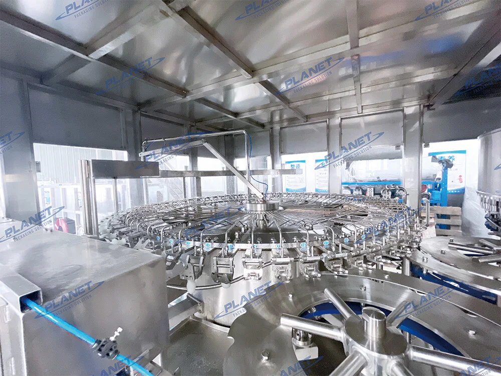 Inside the PET water filler showing the rotary bottle rinsing station and stainless-steel bottle grippers